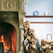 5 Tips for Preserving the Life of Your Fireplace & Chimney Firewood stacked against a wall in a home that is properly preserving the life of their fireplace that is also burning well