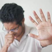 What’s That Smell? 5 Side Effects of Uncleaned Ductwork Person holding up their hand and coughing due to uncleaned air from polluted ductwork.
