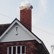 Chimney Cleaning for Different Seasons: What You Need to Know & Do A smoking chimney on top of a residential house in northern virginia that would need chimney cleaning in different seasons.