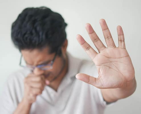 Person holding up their hand and coughing due to uncleaned air from polluted ductwork.