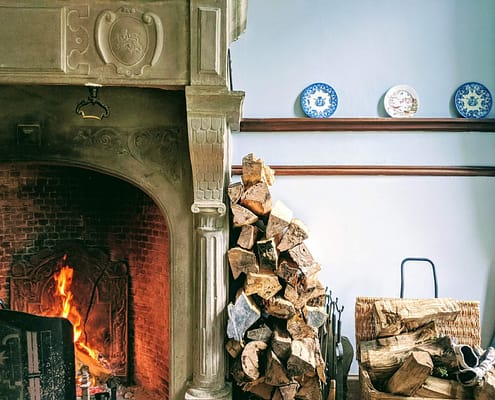 Firewood stacked against a wall in a home that is properly preserving the life of their fireplace that is also burning well