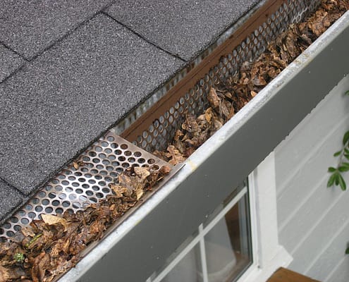 A dirty, clogged gutter causing home problems as a result of not cleaning gutters regularly.