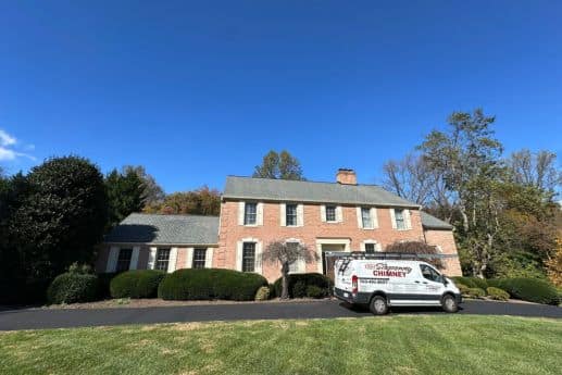 chimney sweep near me alexandria va Brick colonial house with slate roof, manicured shrubs, sunny blue sky, white service van parked front.