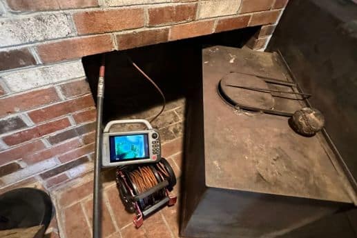 chimney sweep services near me alexandria va Brick fireplace nook with a small TV, a coil of copper wire, and a metal wood stove nearby.