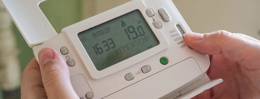 A person holding their thermostat control examining it for any HVAC myths.